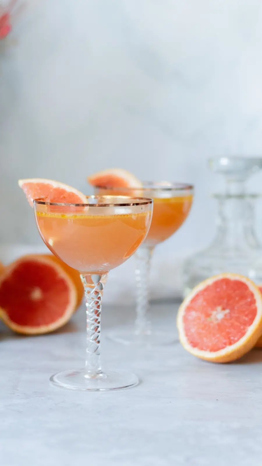 Dos copas de cóctel de pomelo con borde dorado y mitades de pomelo