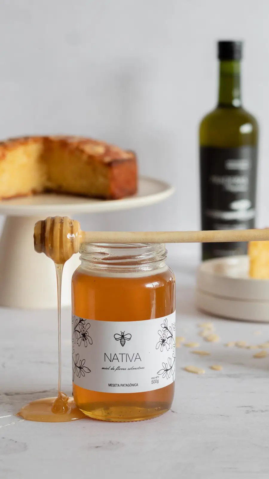 Torta cortada sobre un pie crema junto a un frasco de miel Nativa con cuchara mielera
